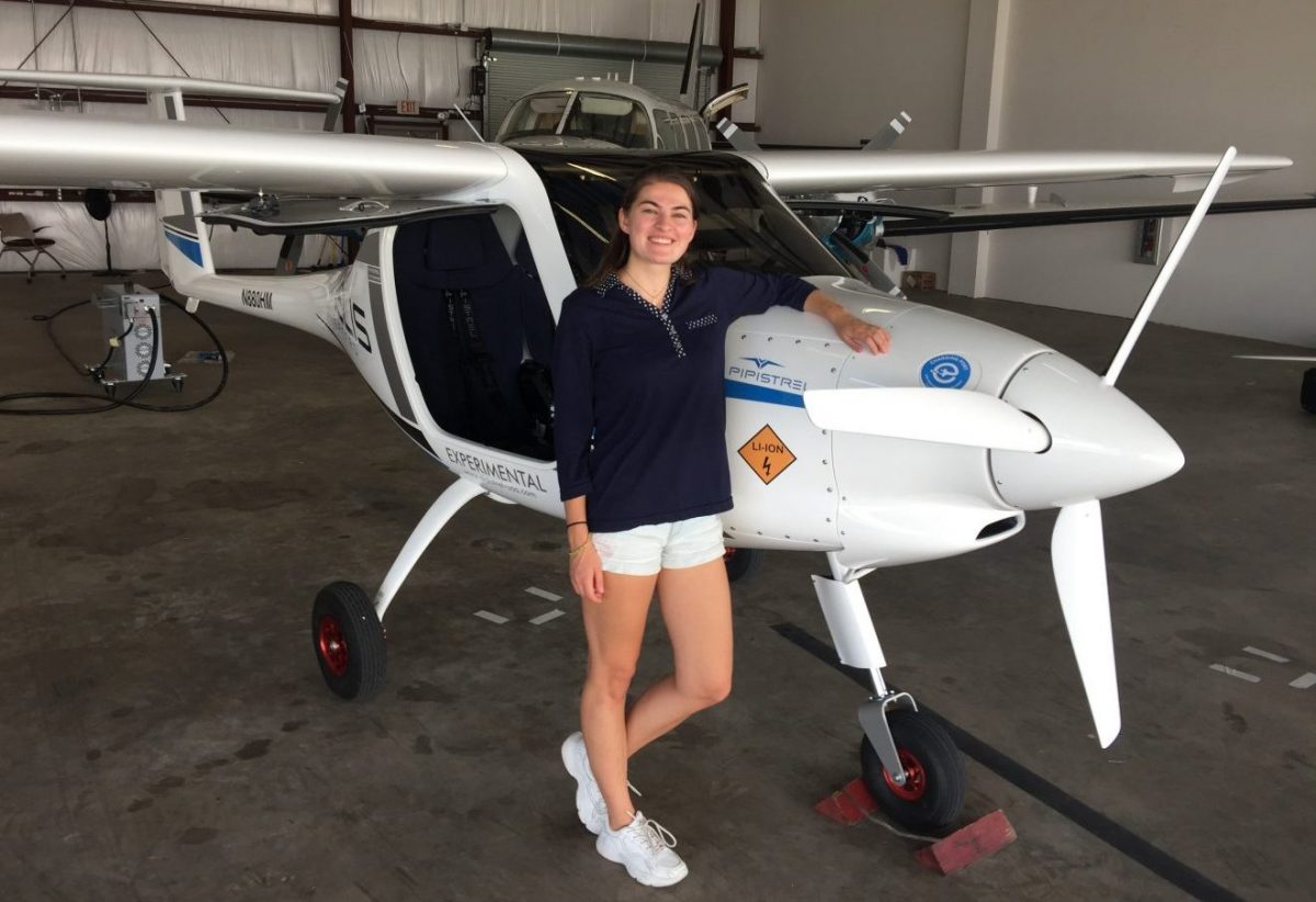 Florida Tech student Elise Medhus leans on the front of the Velis Electro airplane inside a hangar.