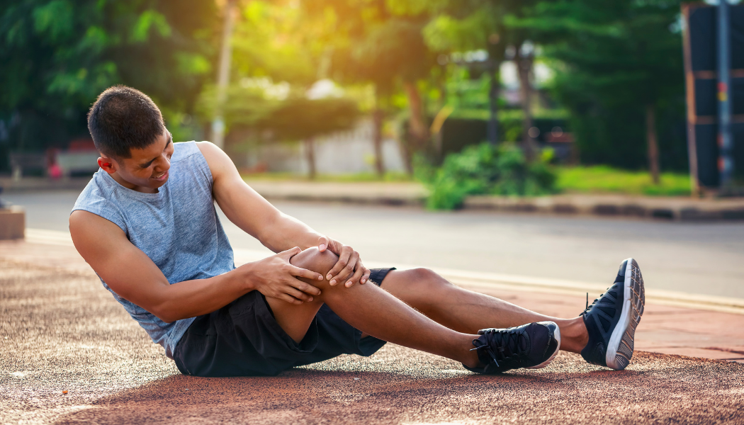 Stock image of a man sitting on the sidewalk holding his knee in pain