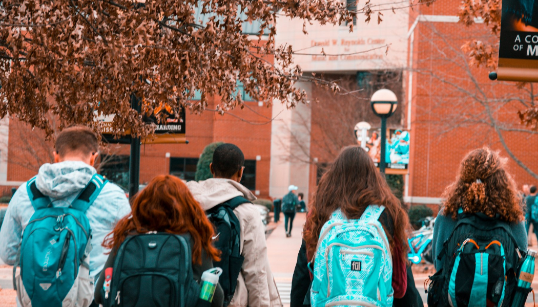 Group of students with backpacks walking away from the camera toward a campus building