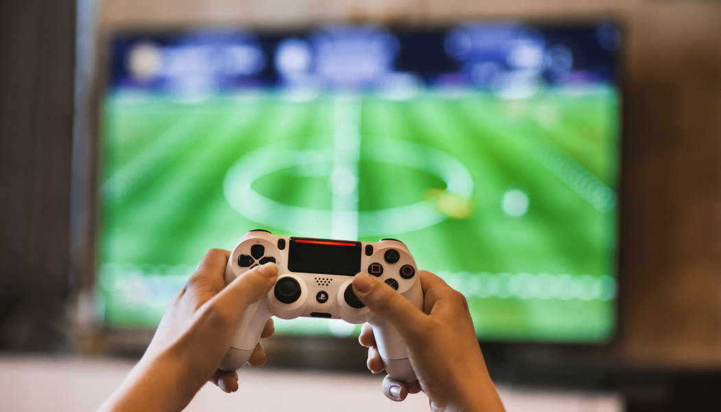 Video game controller being held up by two hands in front of a TV