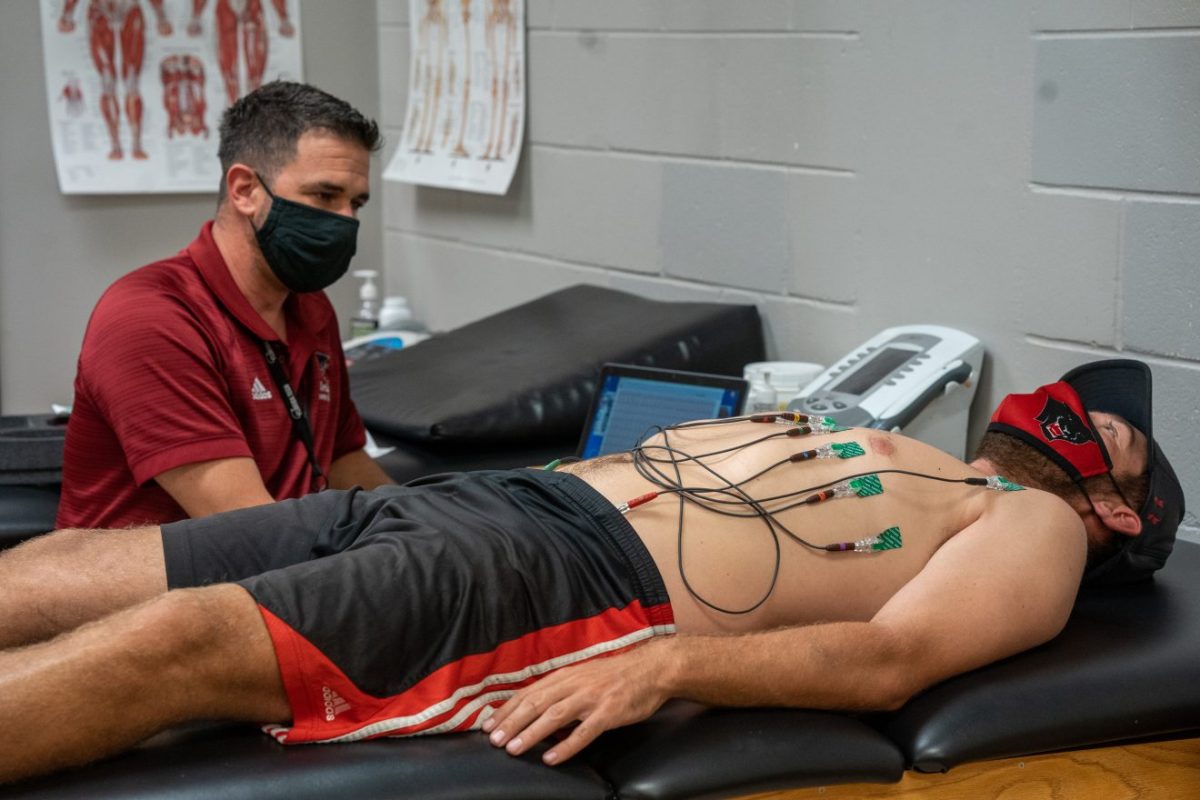 A student-athlete lies on a table connected to an ECG machine with a Florida Tech Athletics trainer beside him.