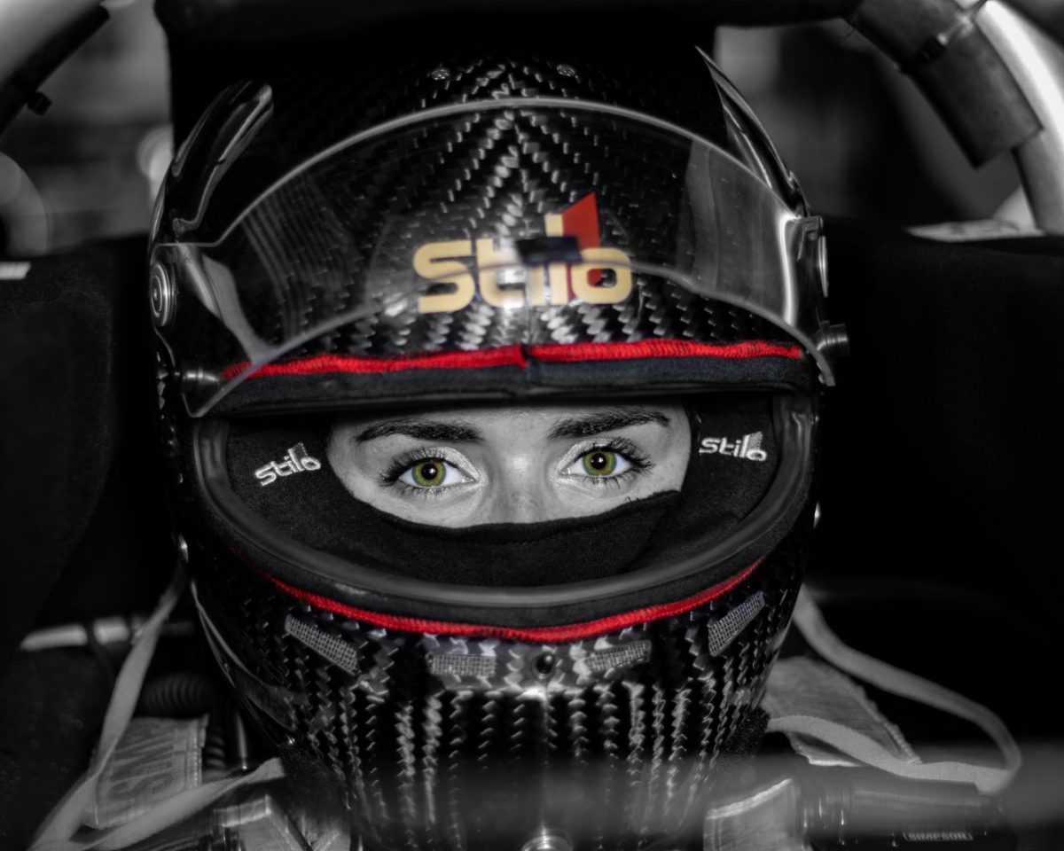 the picture shows a woman's head wearing a racing helmet, its visor raised