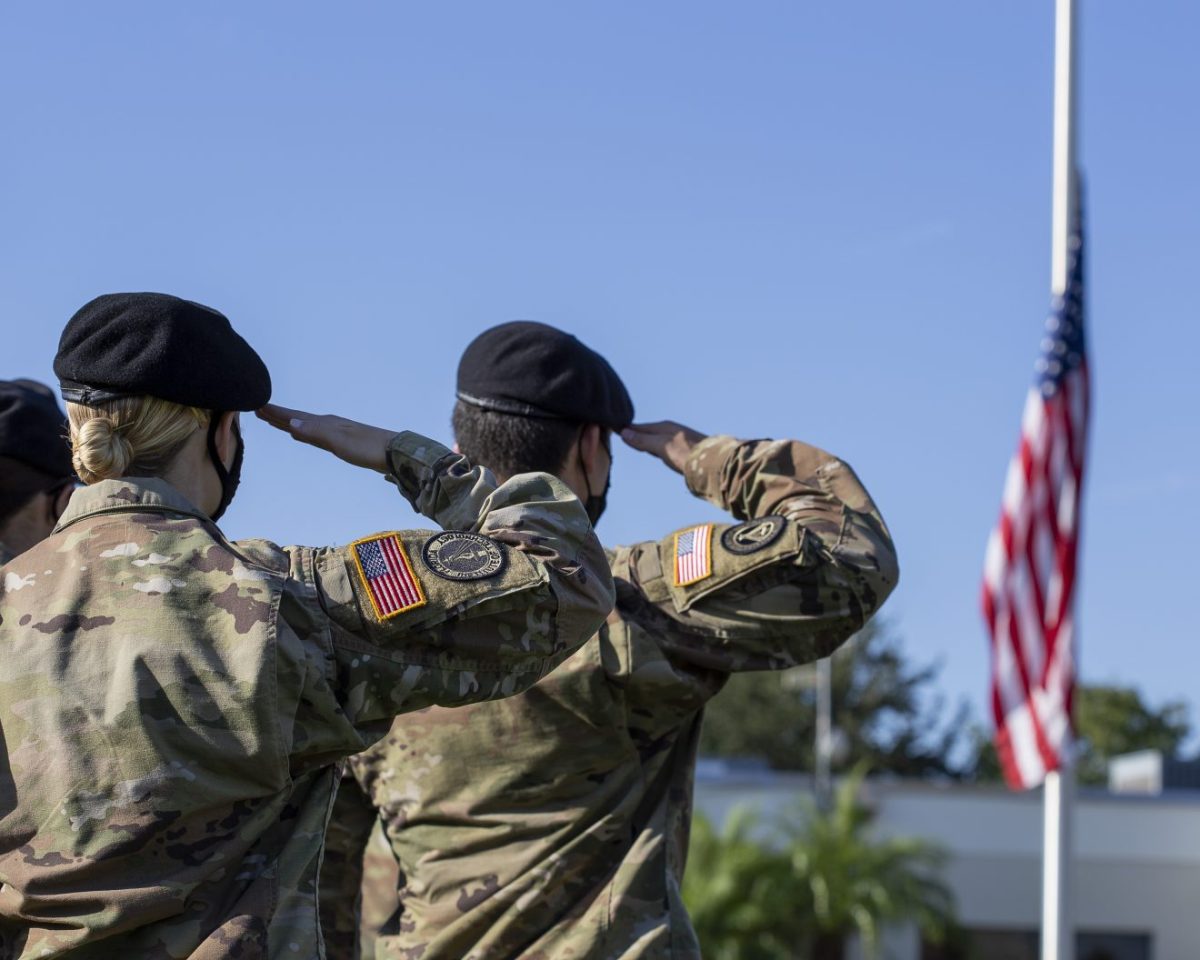 Two ROTC cadets, their backs to the camera, salute a U.S. flag hanging on a flag pole.