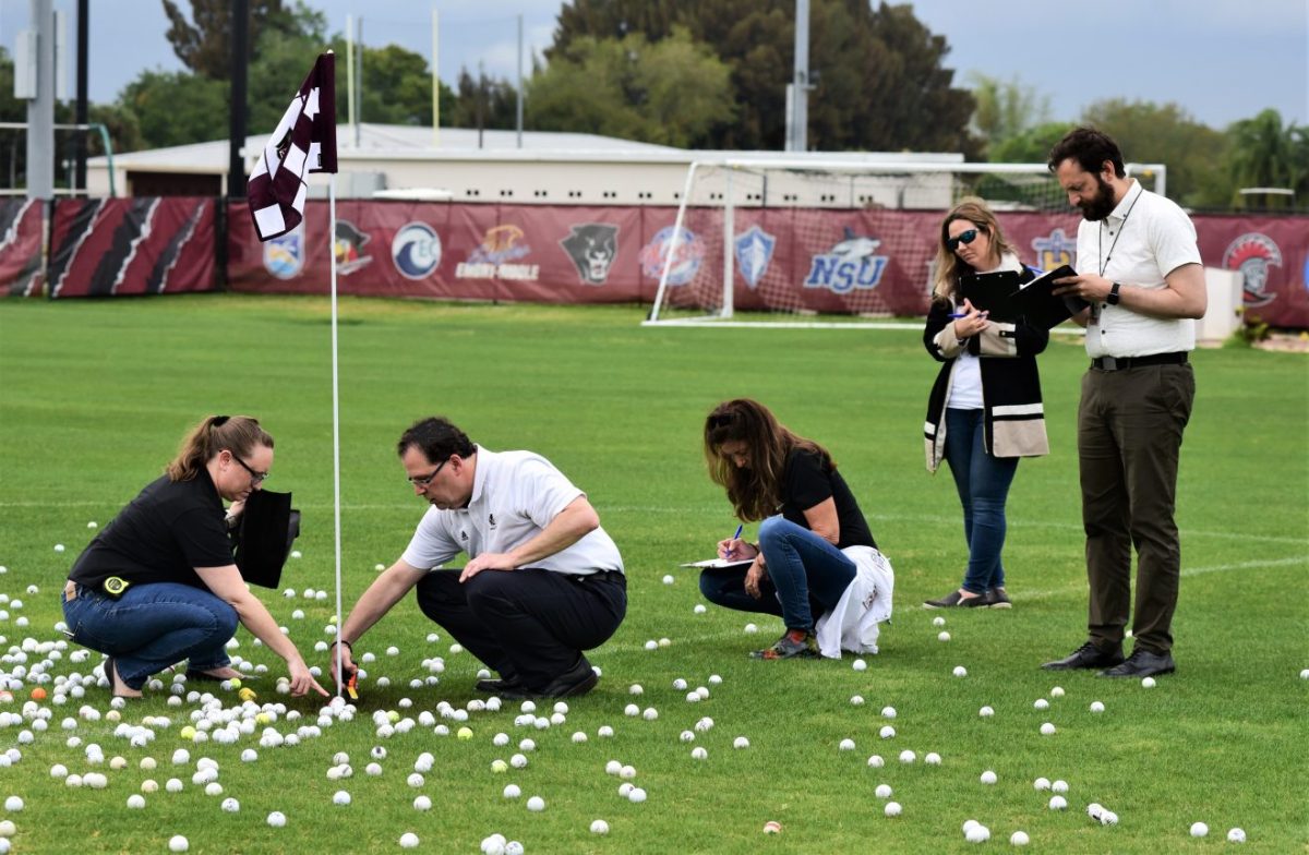 People on a green sports field measuring golf ball distances to the pin.